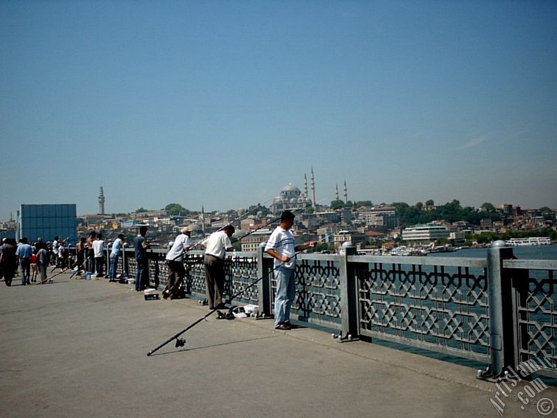 View of fishing people, on the horizon Beyazit Tower and Suleymaniye Mosque from Galata Bridge located in Istanbul city of Turkey.
