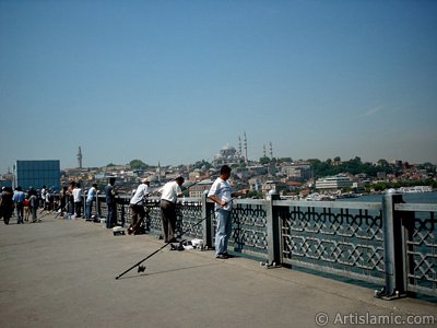 View of fishing people, on the horizon Beyazit Tower and Suleymaniye Mosque from Galata Bridge located in Istanbul city of Turkey. (The picture was taken by Artislamic.com in 2004.)