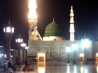 A nighttime view from the outside court of the Prophet Muhammad`s (saaw) Mosque (Masjed an-Nabawe) in Madina city of Saudi Arabia. On the area under the green dome there are tombs of the Prophet Muhammad, Abubakr (first caliph of Islam) and Omar (second caliph). At the same time there is home and minbar of the Prophet and ``soffa`` where the poor muslims used to stay and take education in the time of the Prophet. When you enter from the door in your front, after taking a few steps, on the rigth you will find the home and tomb of the Prophet Muhammad (saaw). (The picture was taken by Mr. Mustafa one of the visitors of Artislamic.com in 2003 Ramadan.)
